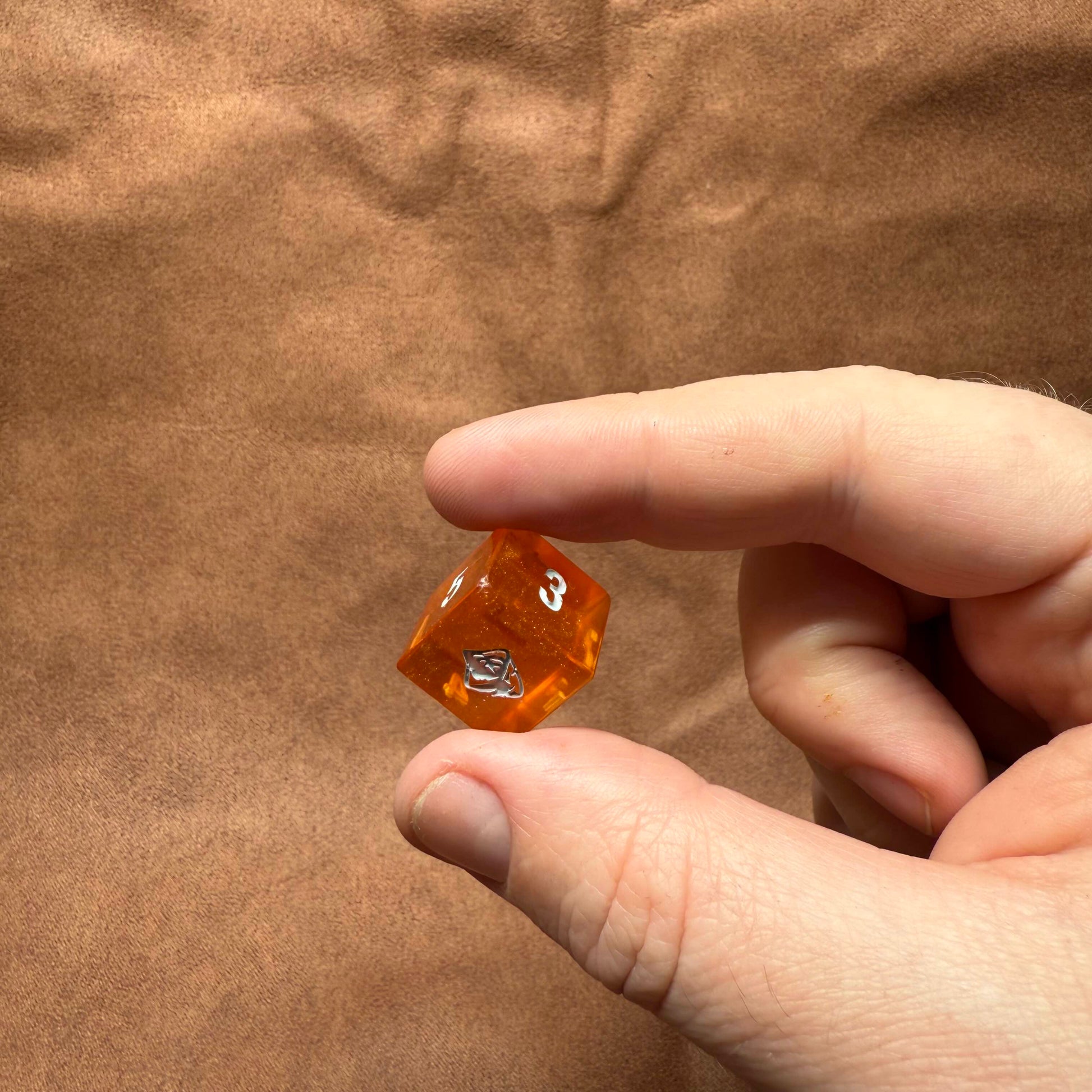 Hand holding an orange die with a brown background