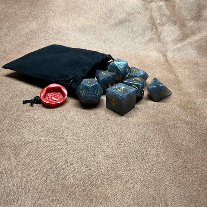 Set of polyhedral dice with a black drawstring bag and red die on a beige surface