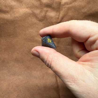 Hand holding a small dark stone with a yellow symbol against a brown background