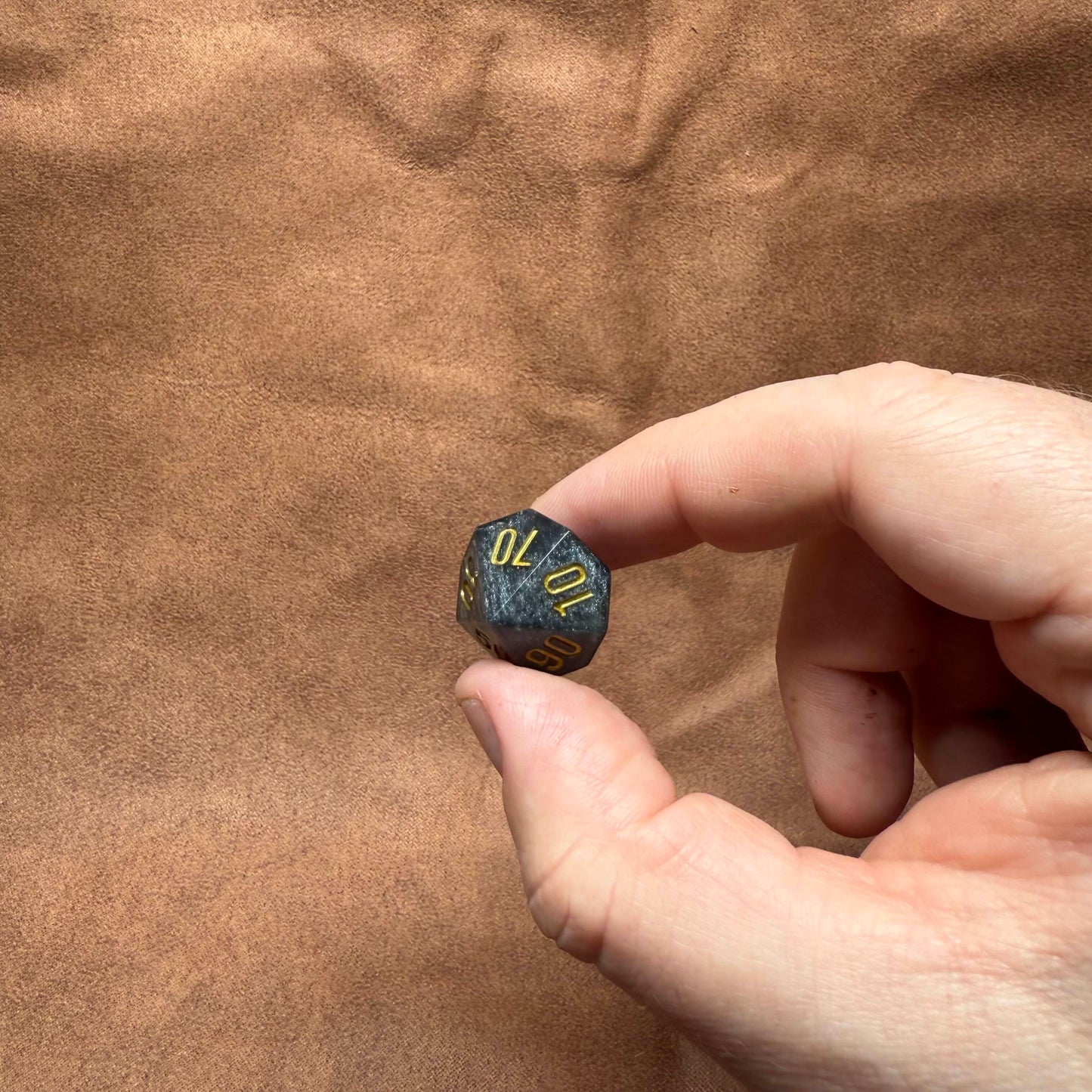 Hand holding a small dice with numbers on a brown fabric background