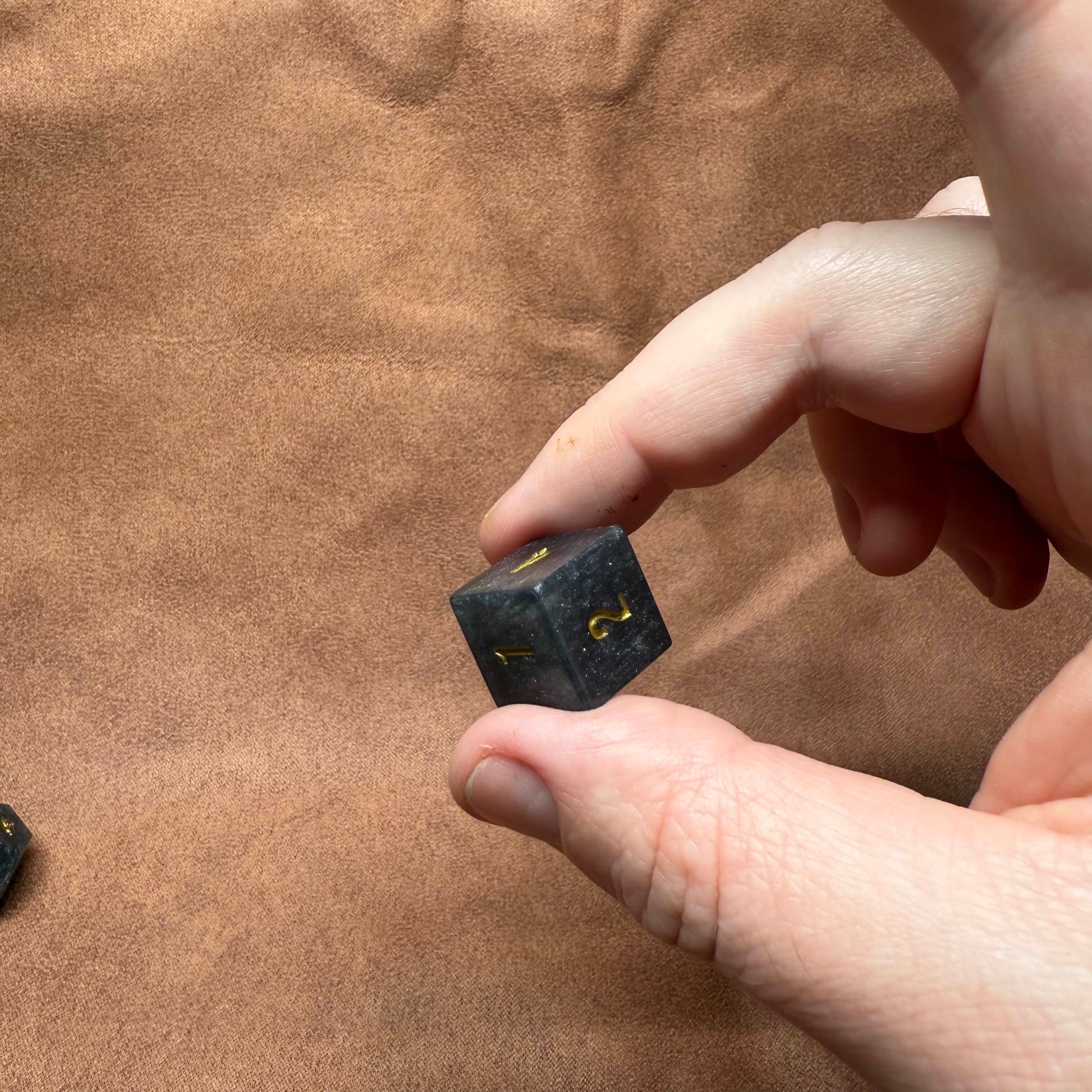 Hand holding a small black object with gold accents on a brown fabric background
