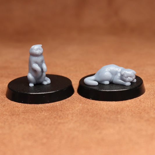 Two miniature cat figurines on black bases against a brown background
