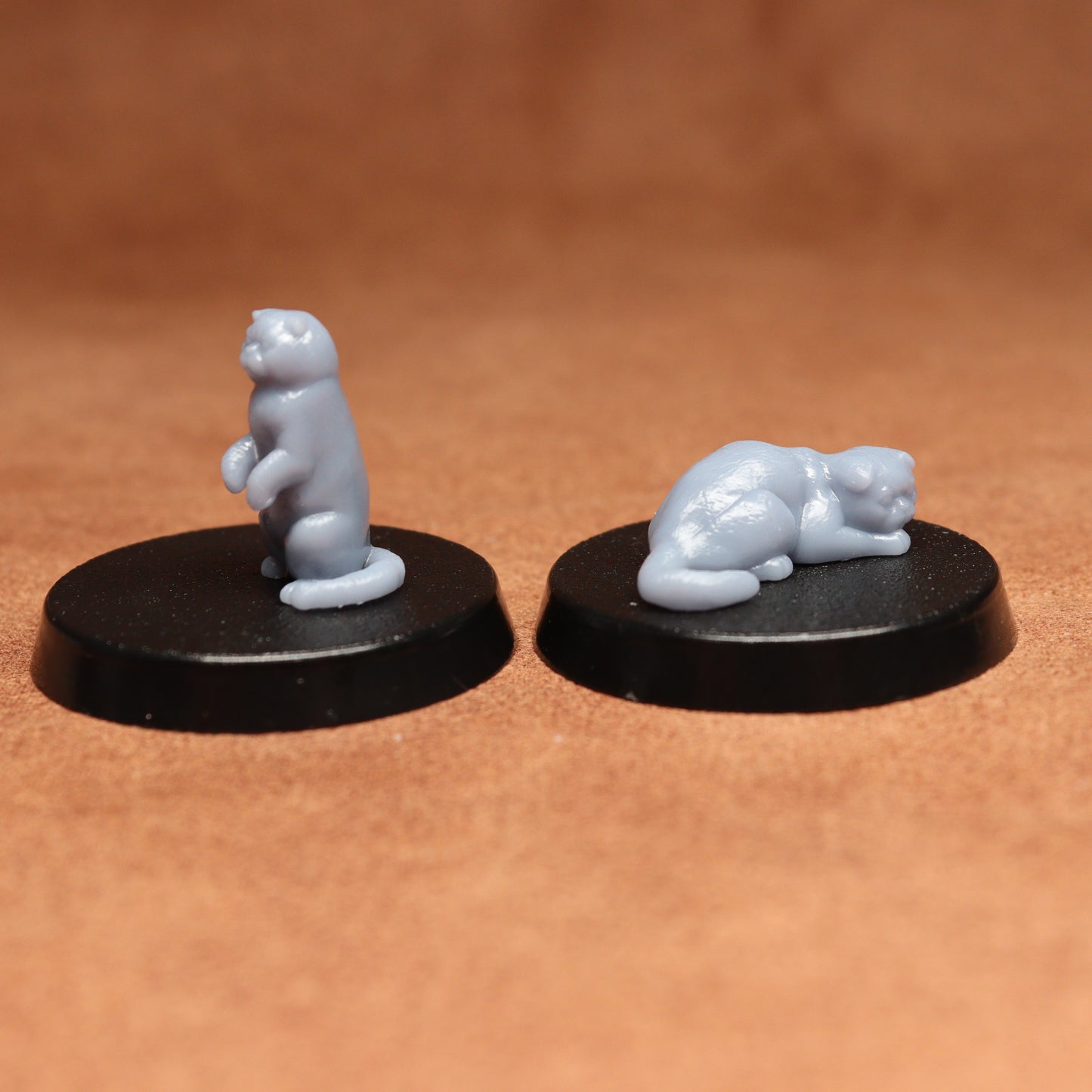Two small cats figurines on black bases against a brown background
