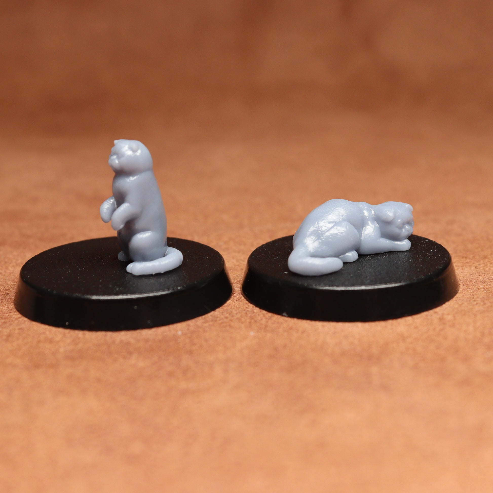 Two small cats figurines on black bases against a brown background