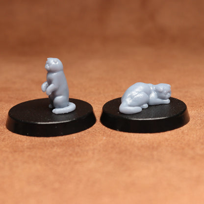 Two small cats figurines on black bases against a brown background