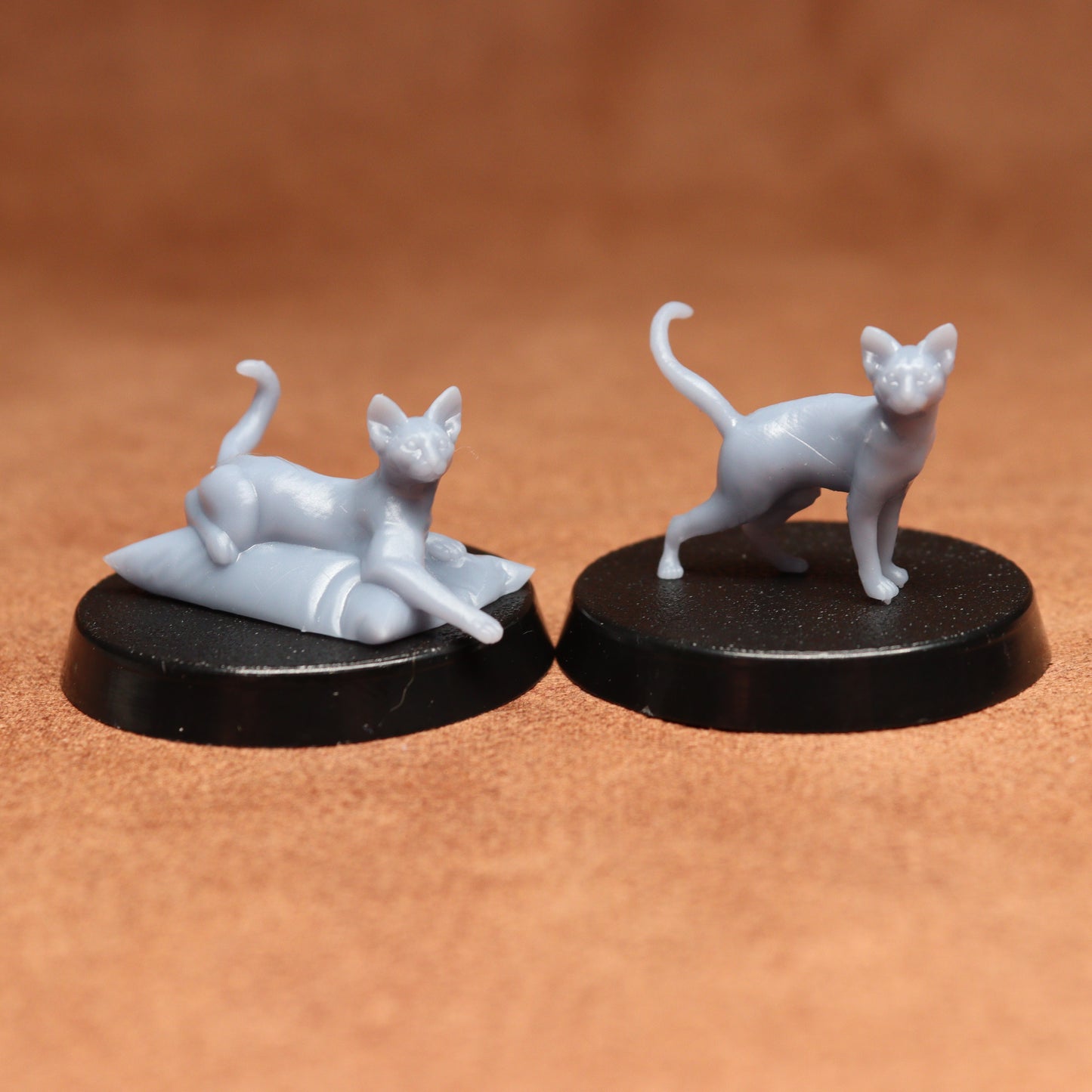 Two white cat figurines on black bases against a brown background
