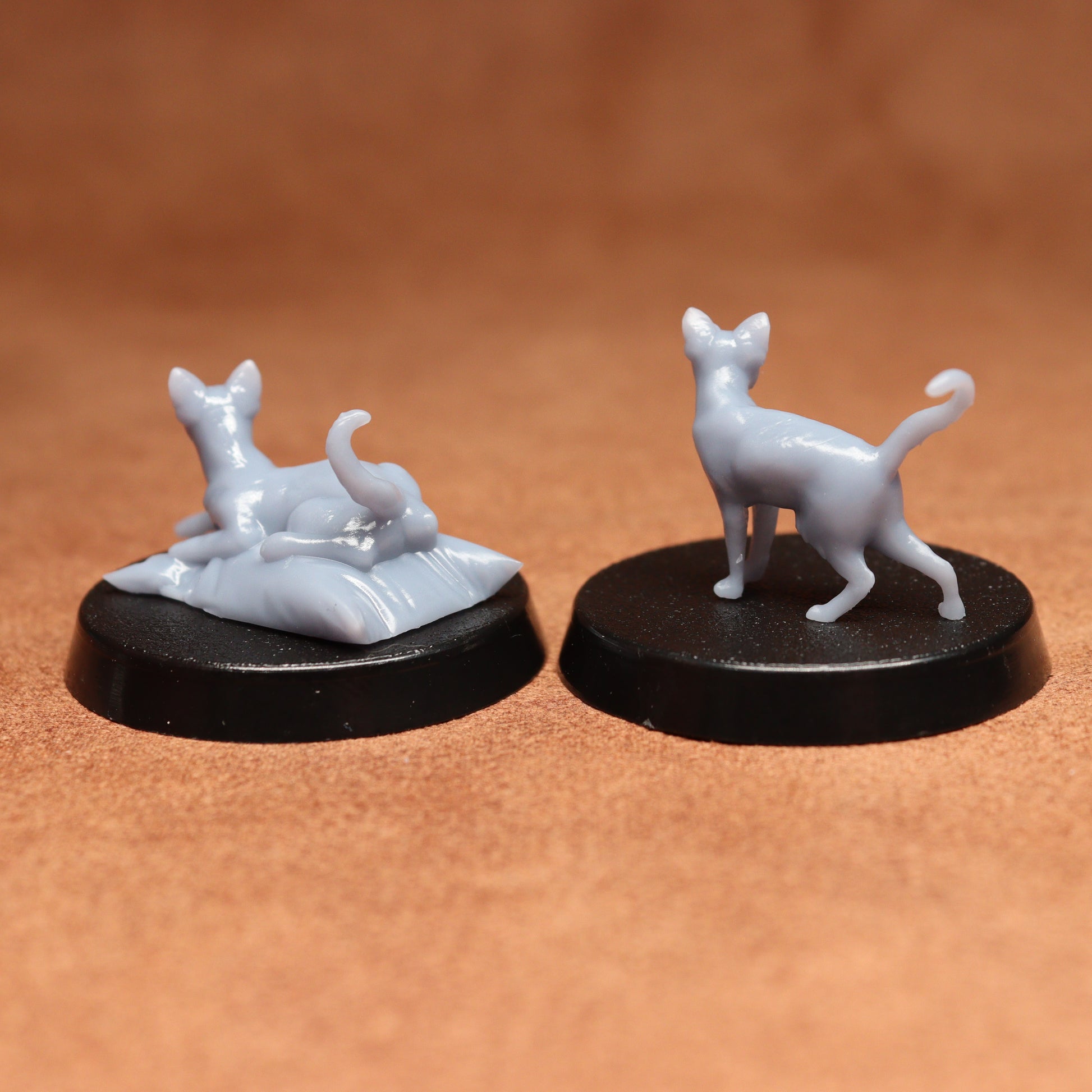 Two miniature cat figurines on black bases against a brown background