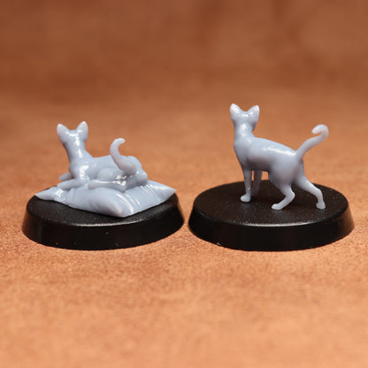 Two miniature cat figurines on black bases against a brown background