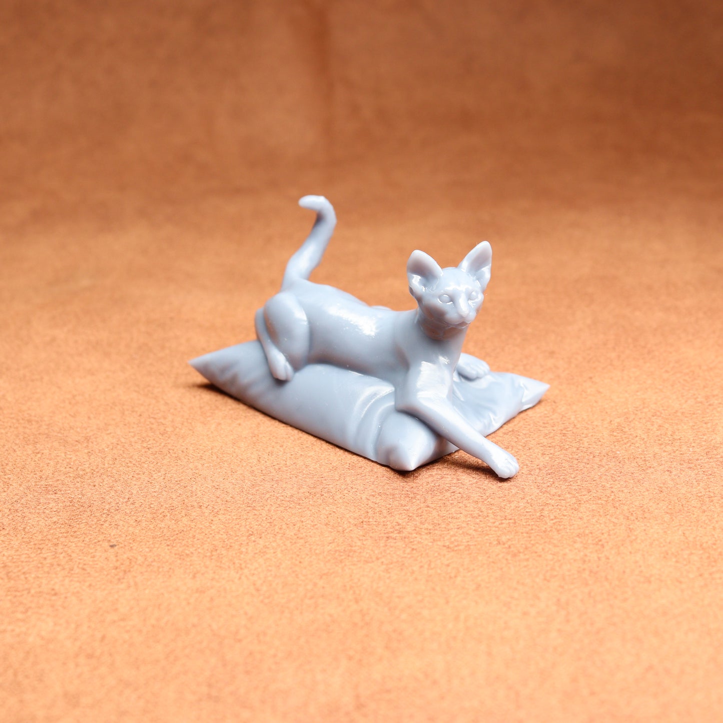 White cat figurine lying on a pillow against an orange background