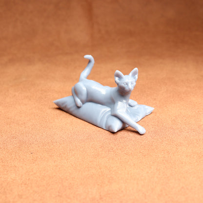 White cat figurine lying on a pillow against an orange background