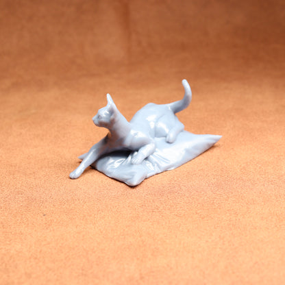 White ceramic sculpture of a cat on a textured brown surface
