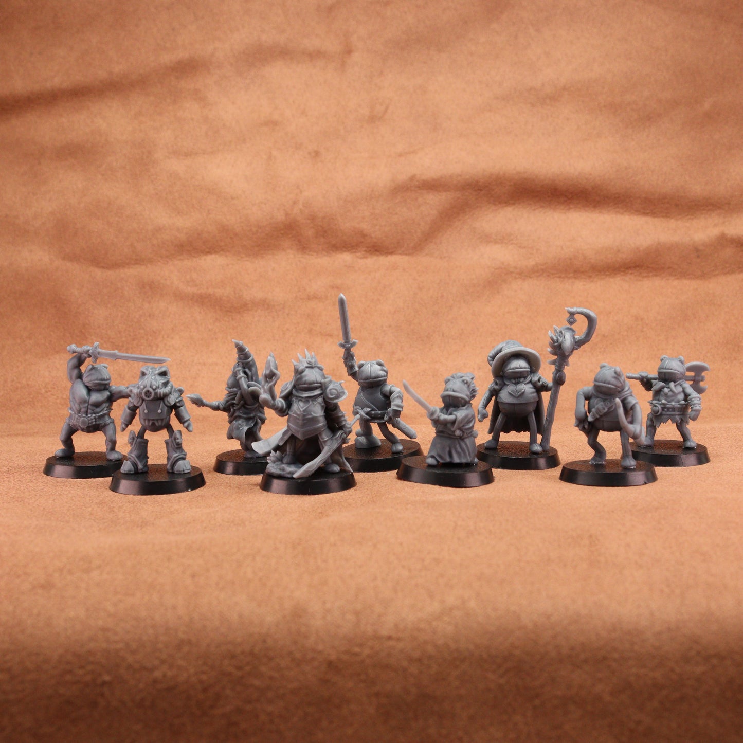 A set of unpainted gray fantasy tabletop miniatures posed in a row on a brown textured fabric background.