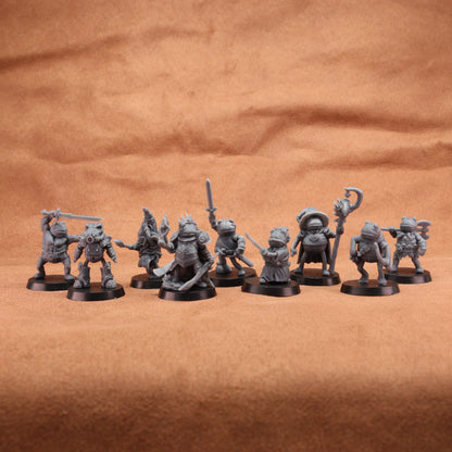 A set of unpainted gray fantasy tabletop miniatures posed in a row on a brown textured fabric background.