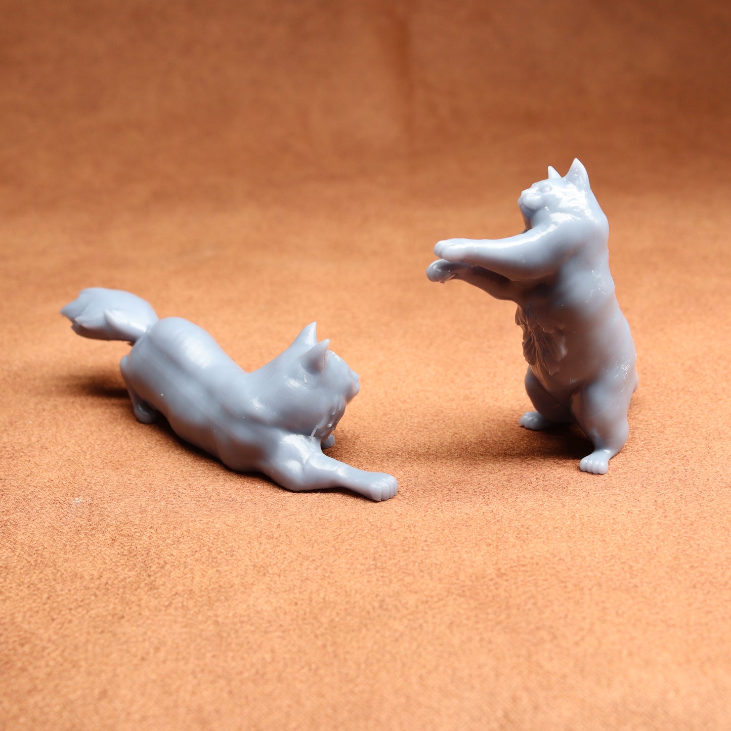 Two white ceramic cat figurines on a brown surface