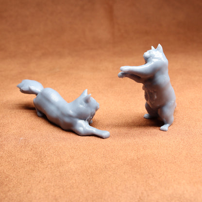 Two white ceramic cat figurines on a brown surface