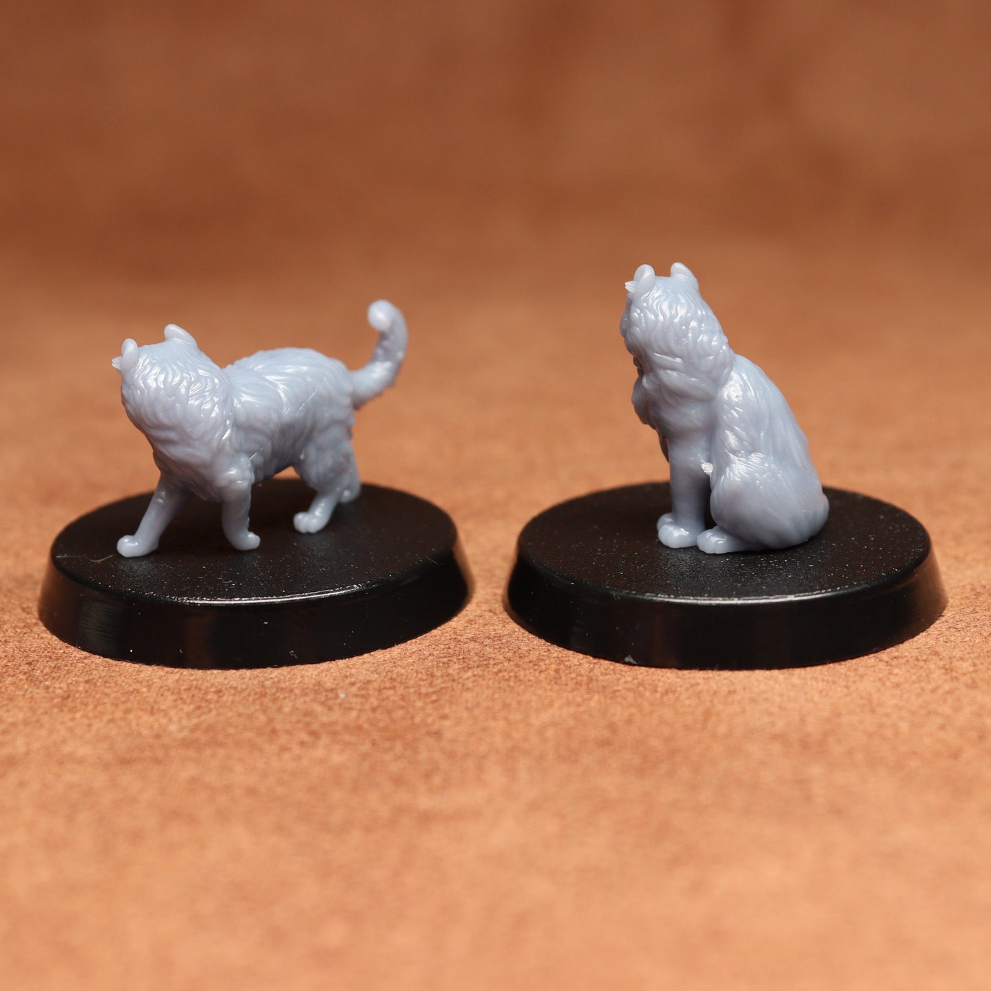 Two miniature cat figurines on black bases against a brown background