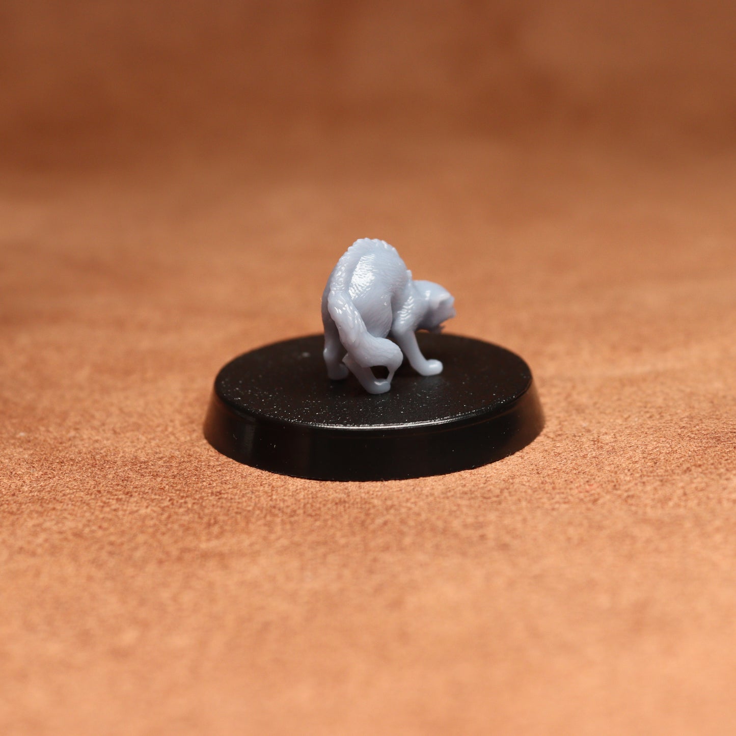 Small gray figurine on a black round base against a brown background