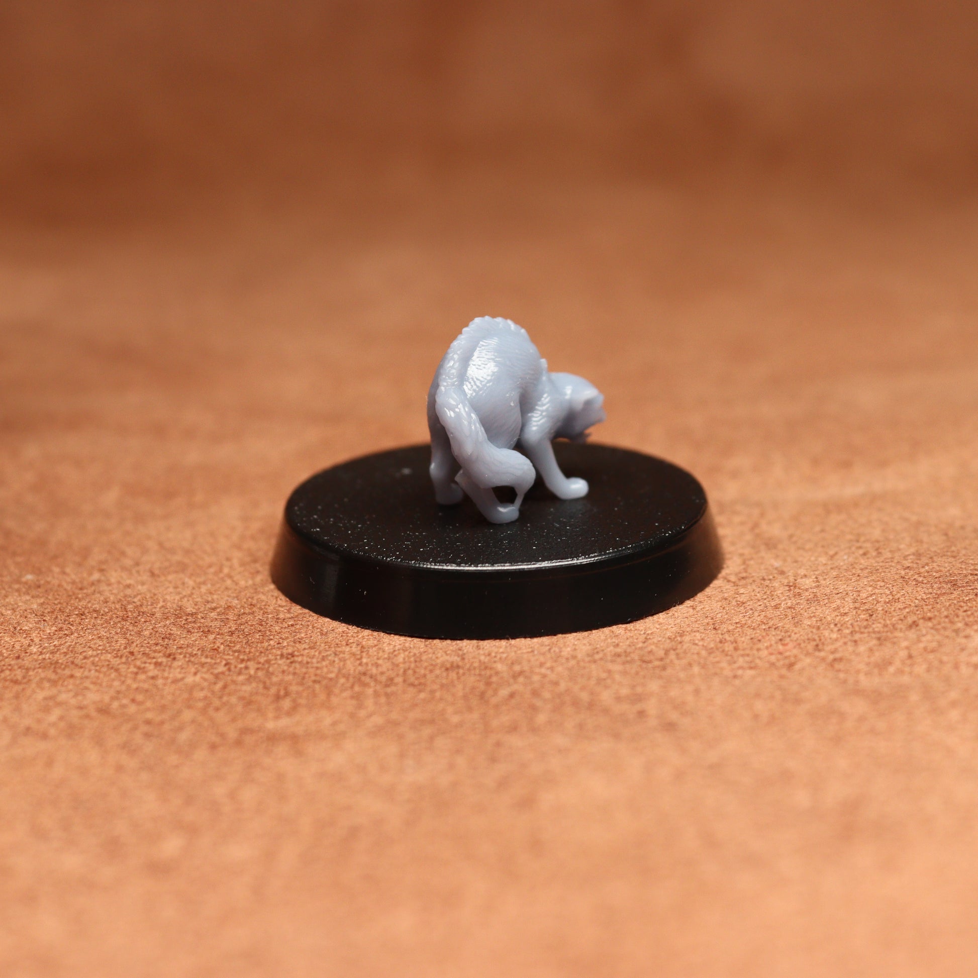 Small gray figurine on a black round base against a brown background