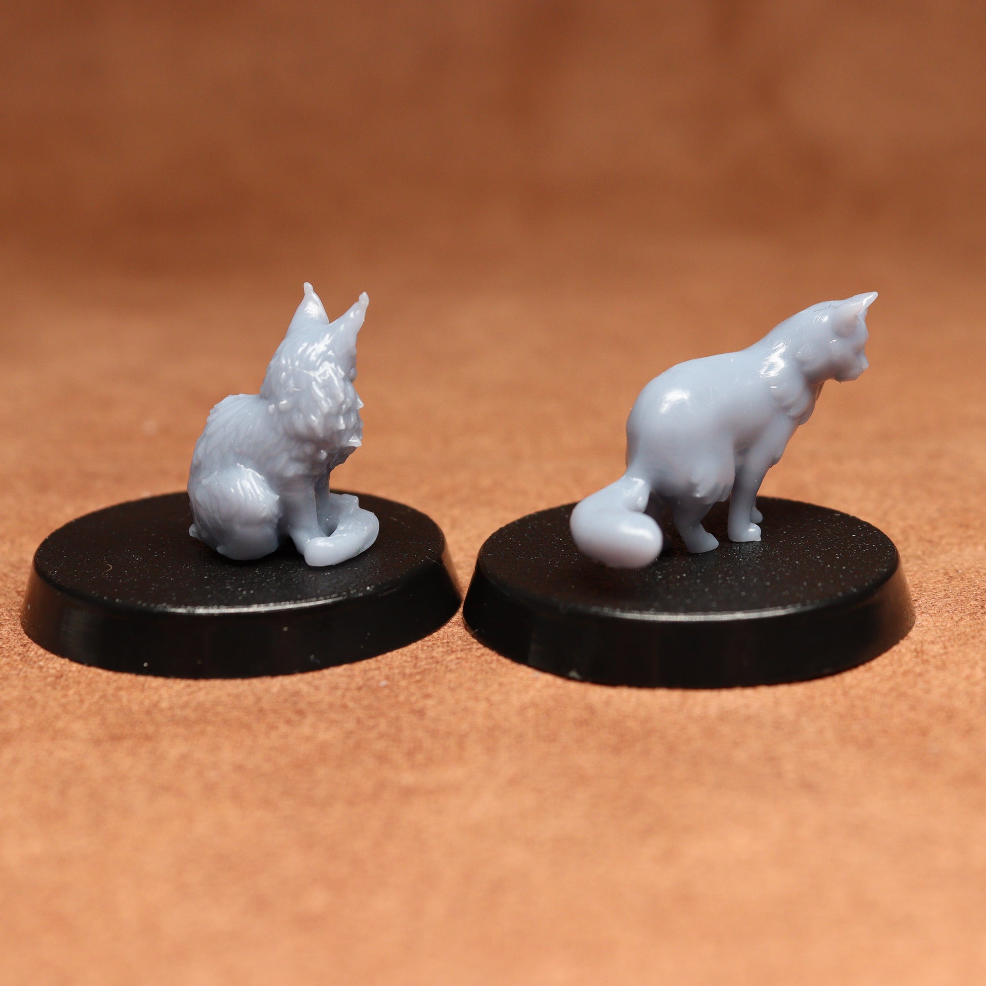 Two white cat figurines on black bases against a brown background