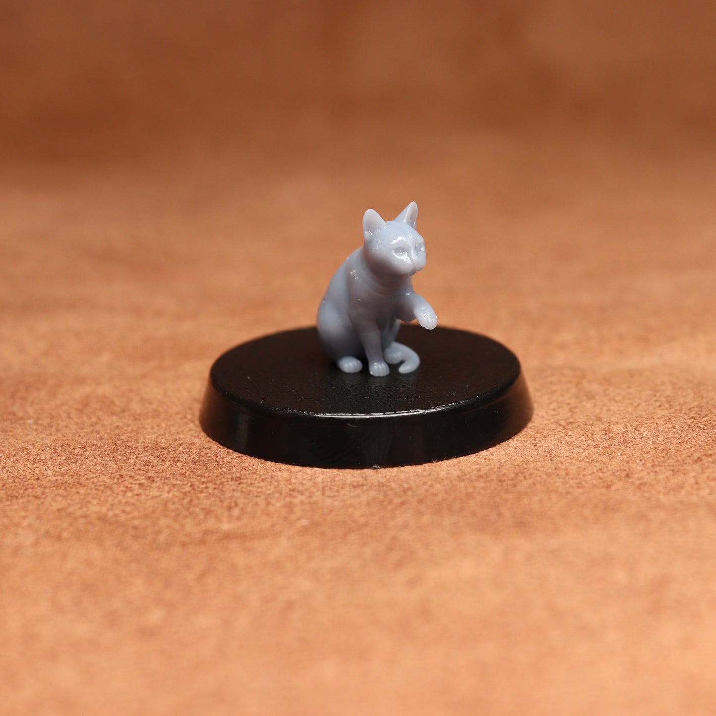 grey resin miniature cat figure on a black base with a brown background