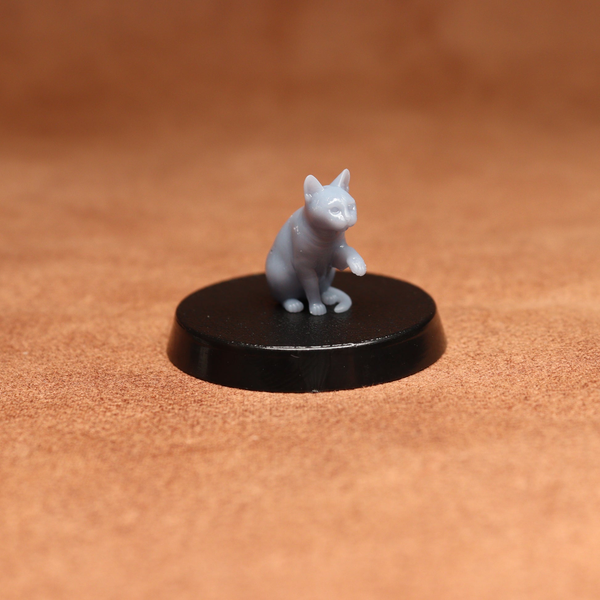 grey resin miniature cat figure on a black base with a brown background