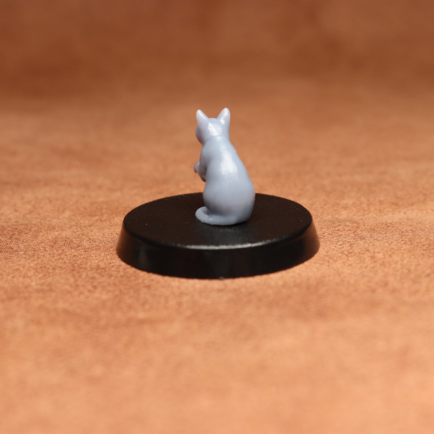 grey resin miniature cat figure on a black base with a brown background