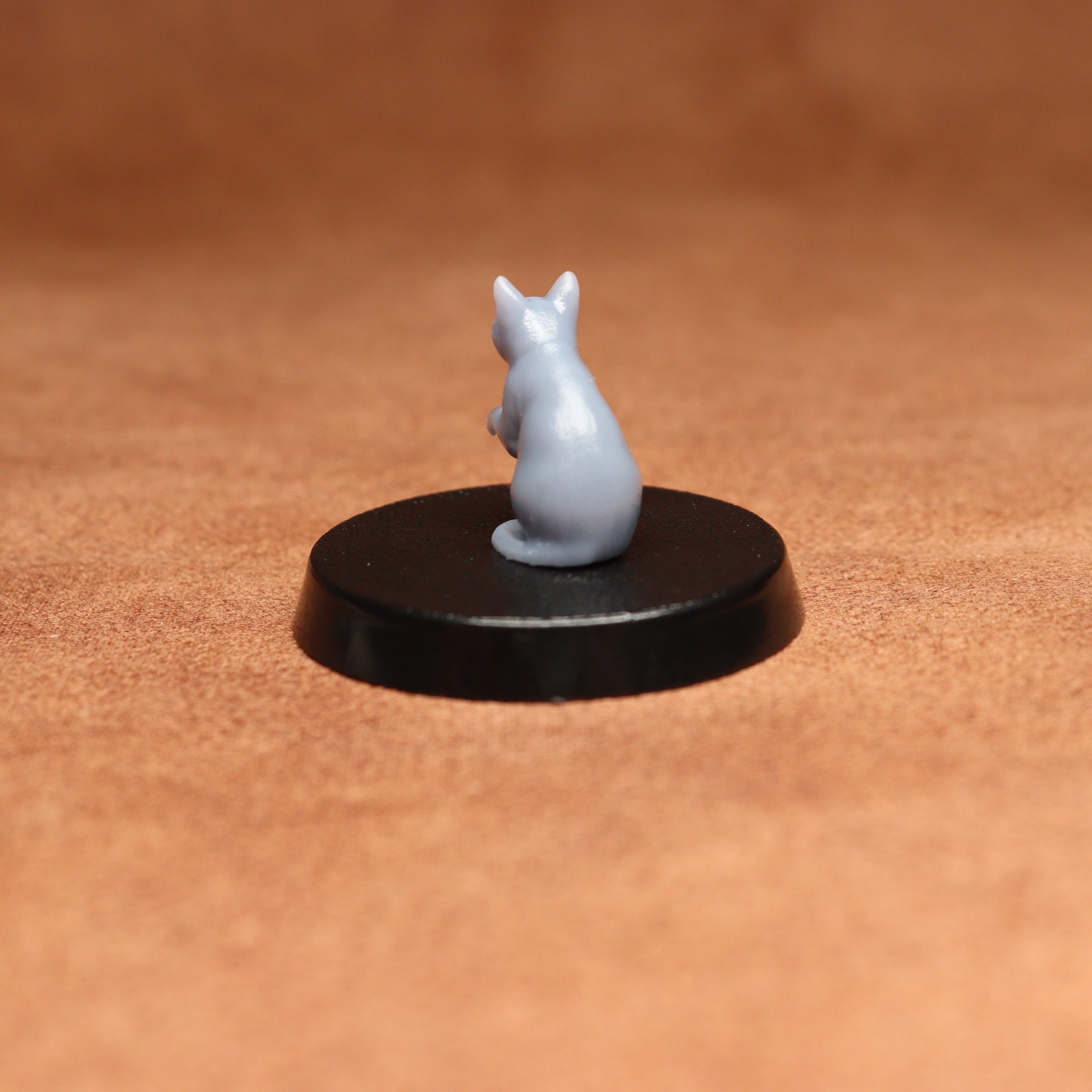grey resin miniature cat figure on a black base with a brown background