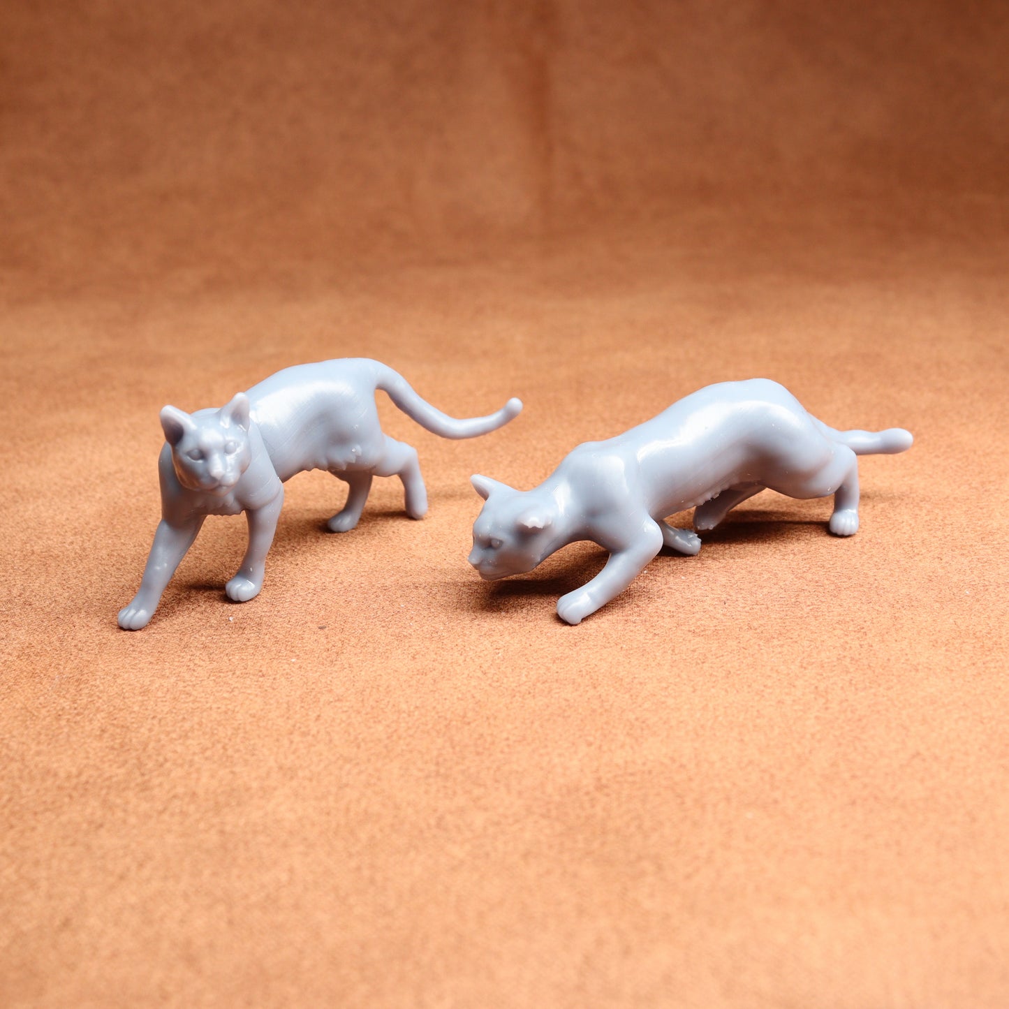 Two white cat figurines on a brown surface