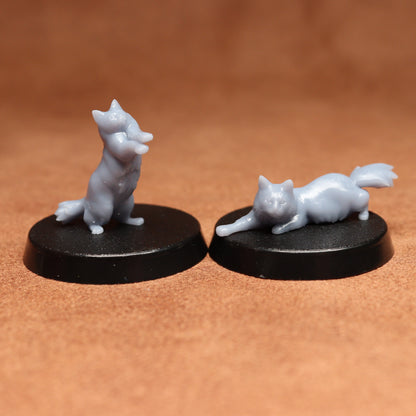 Two small figurines of cats on black bases against a brown background