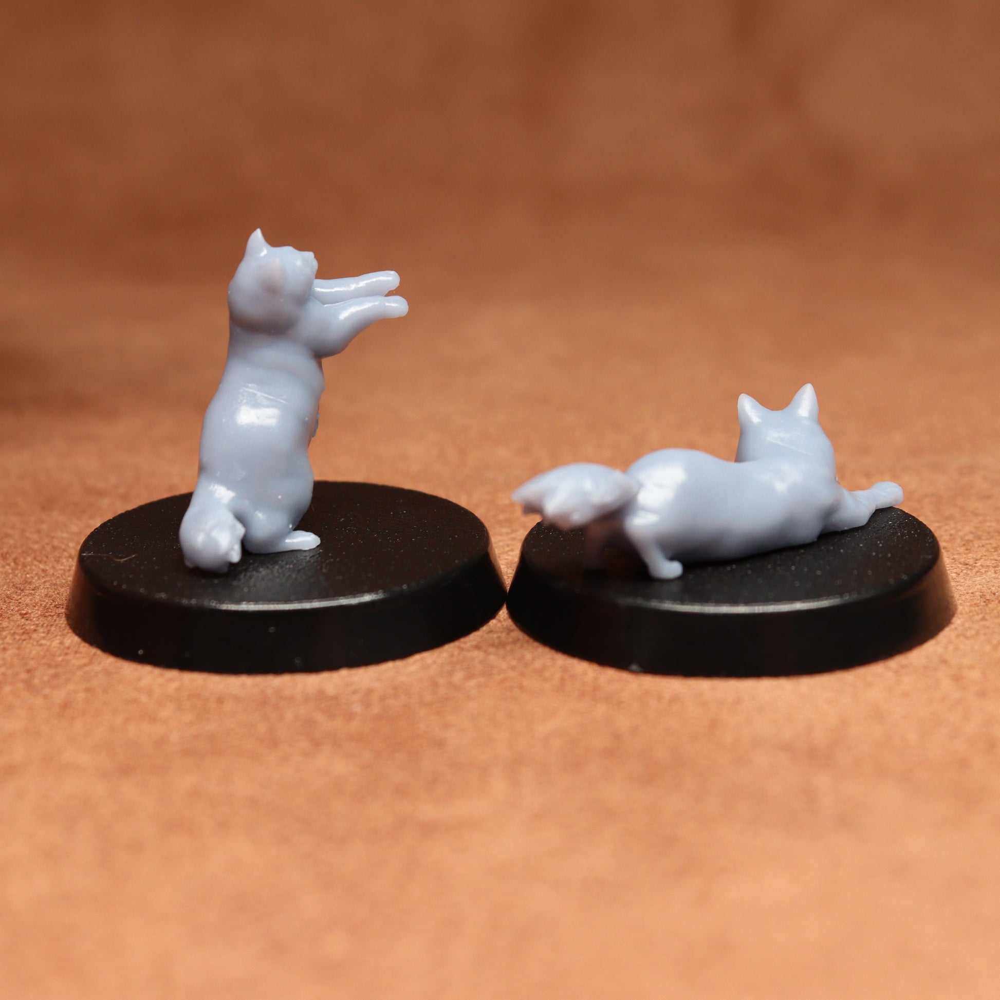 Two white cat figurines on black bases against a brown background