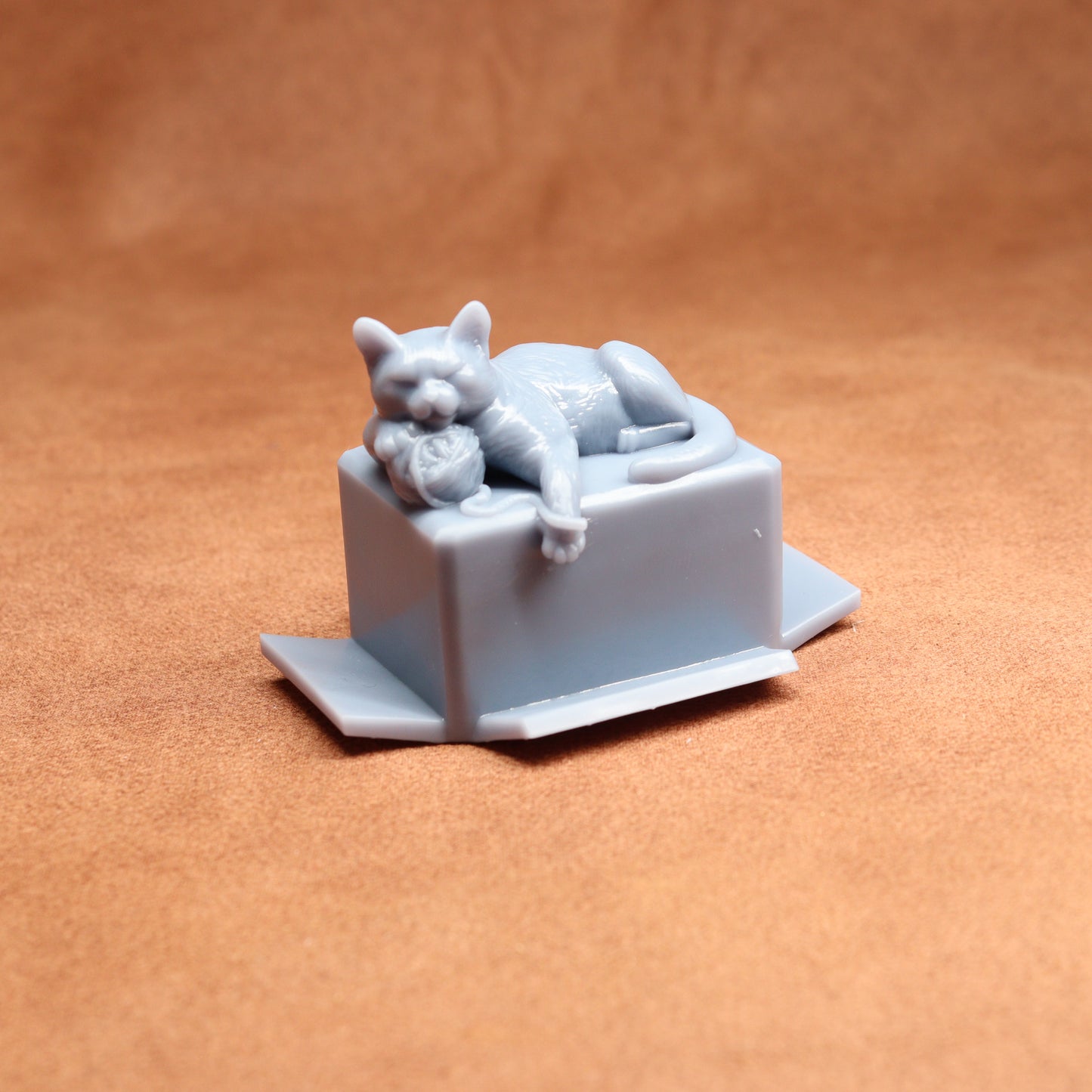 Gray cat figurine laid on a box against a brown background