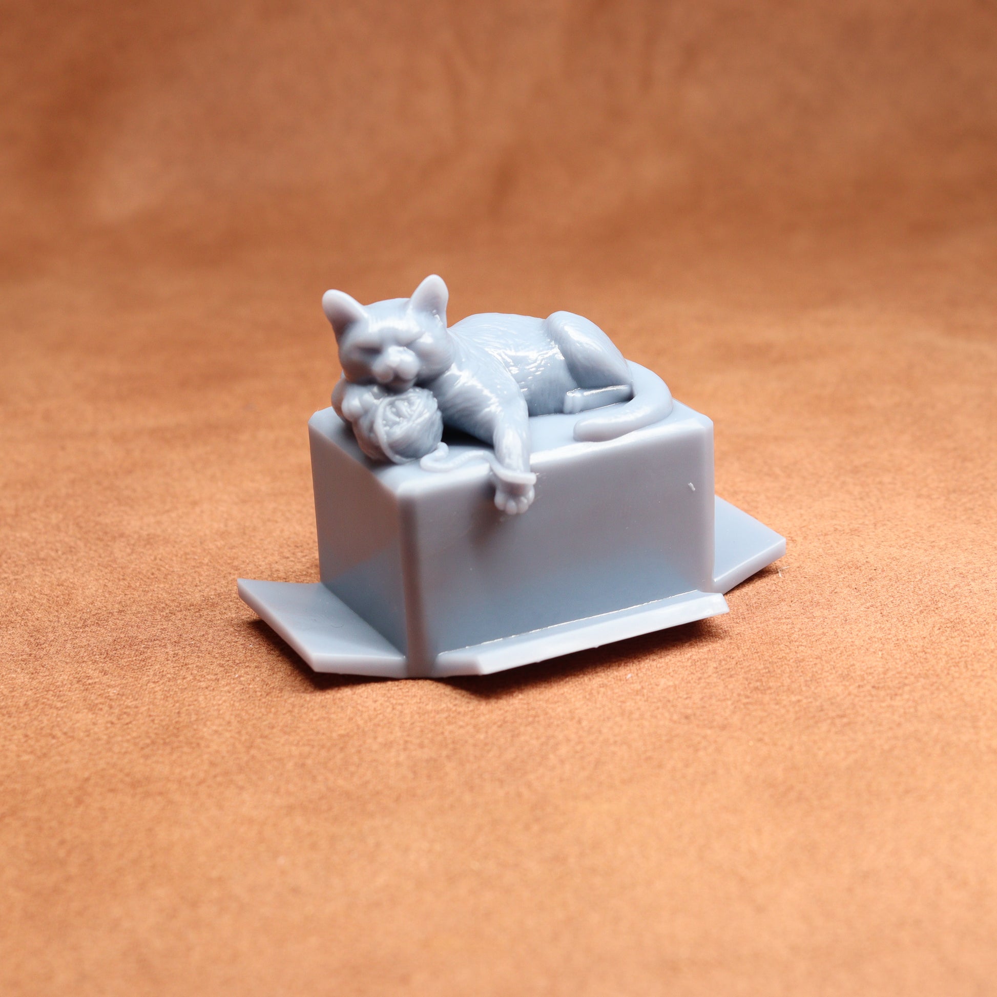 Gray cat figurine laid on a box against a brown background
