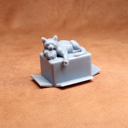 Gray cat figurine laid on a box against a brown background