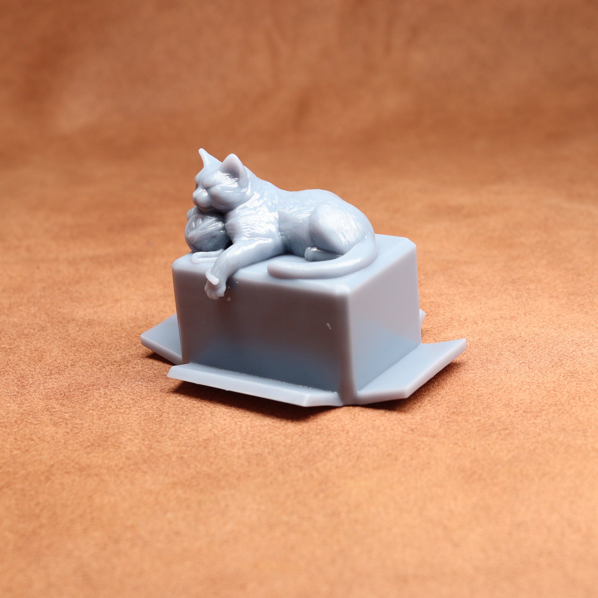 Gray cat figurine laid on a box against a brown background