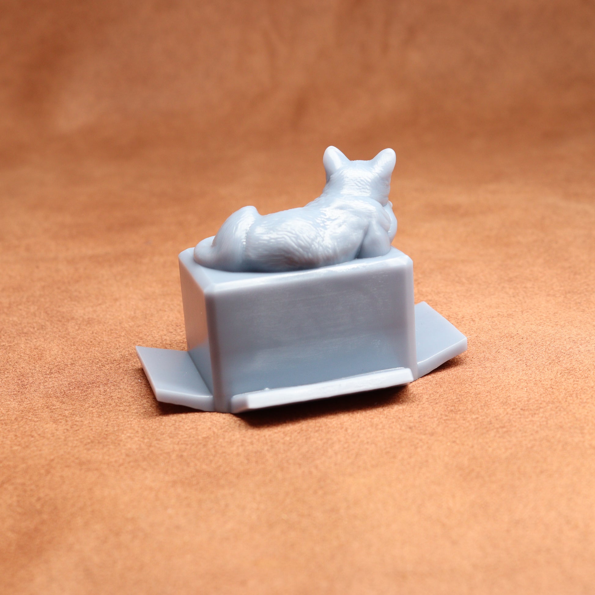 Gray cat figurine laid on a box against a brown background