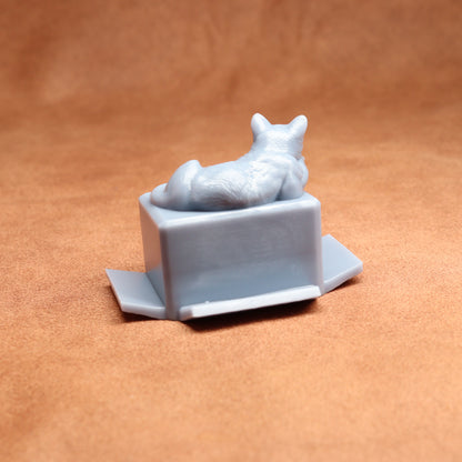 Gray cat figurine laid on a box against a brown background