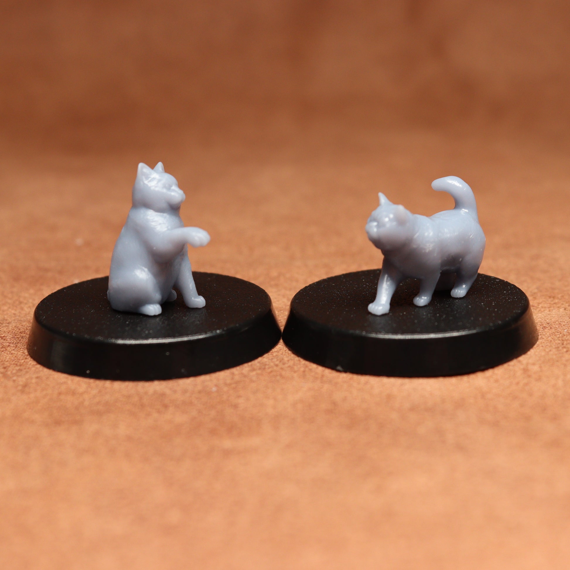 Two miniature cat figurines on black bases against a brown background