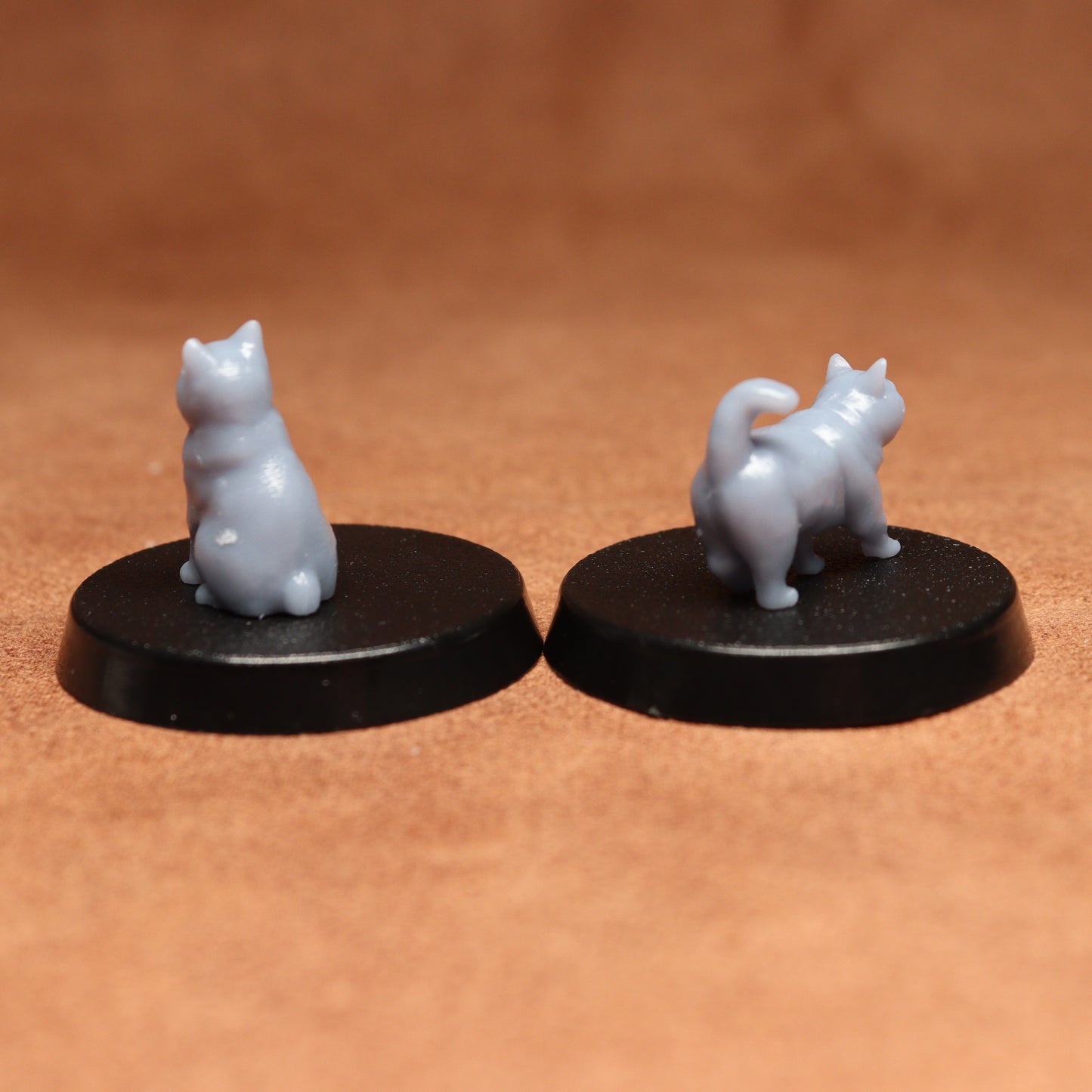 Two miniature cat figurines on black bases against a brown background