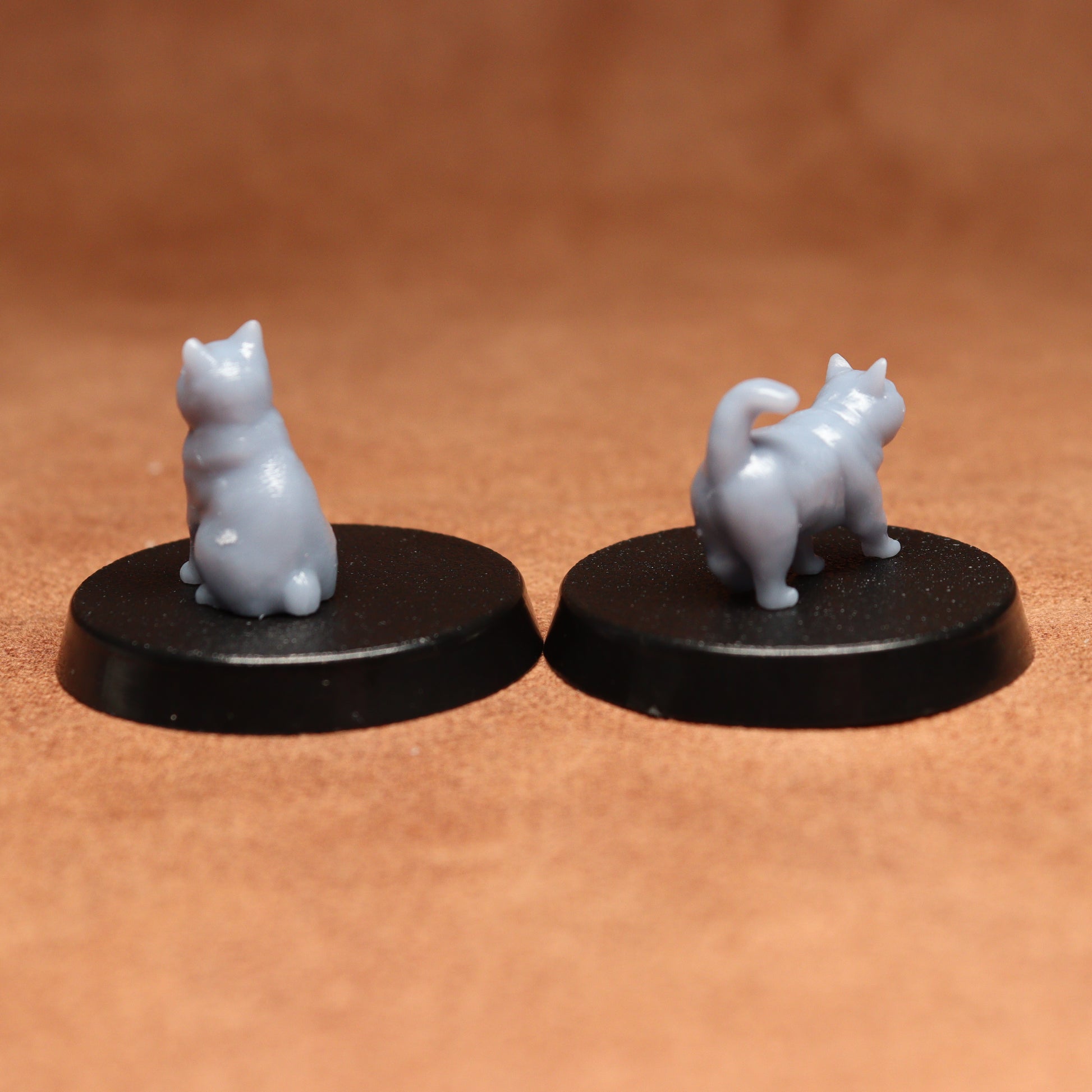 Two miniature cat figurines on black bases against a brown background