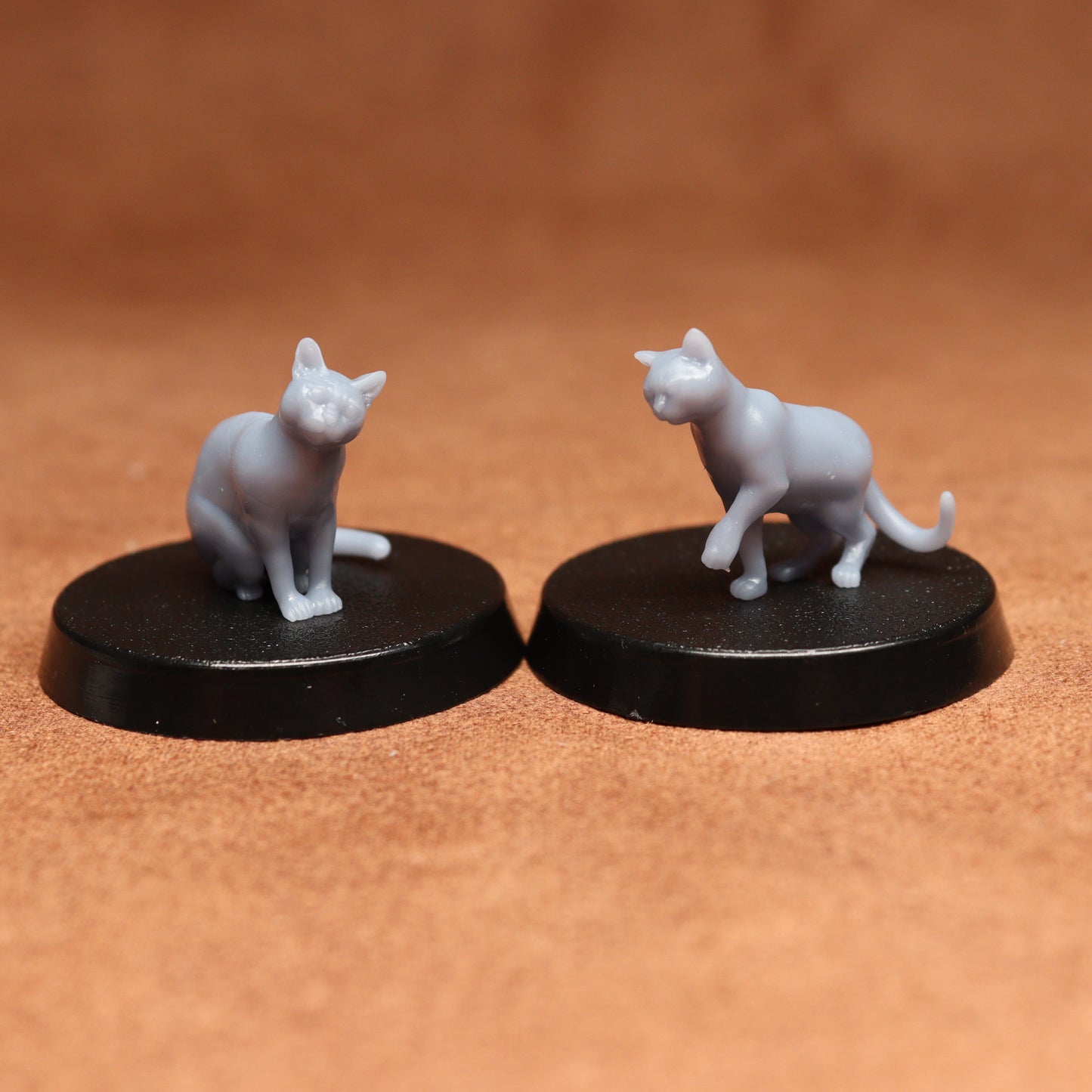 Two miniature cat figurines on black bases against a brown background