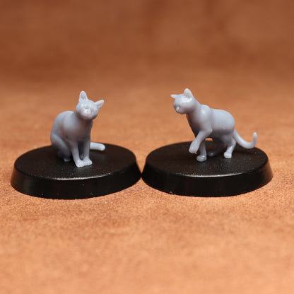 Two miniature cat figurines on black bases against a brown background