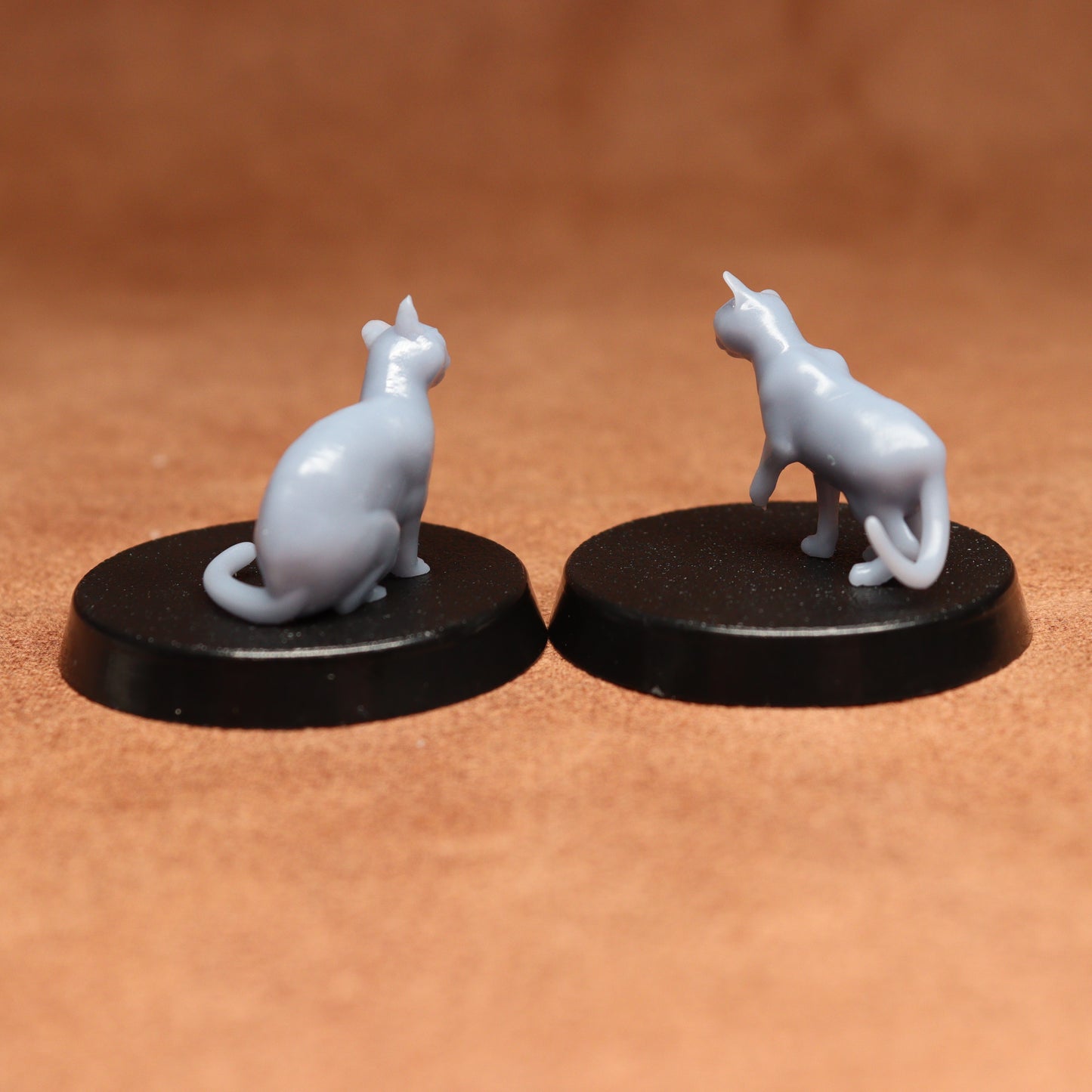 Two miniature cat figurines on black bases against a brown background