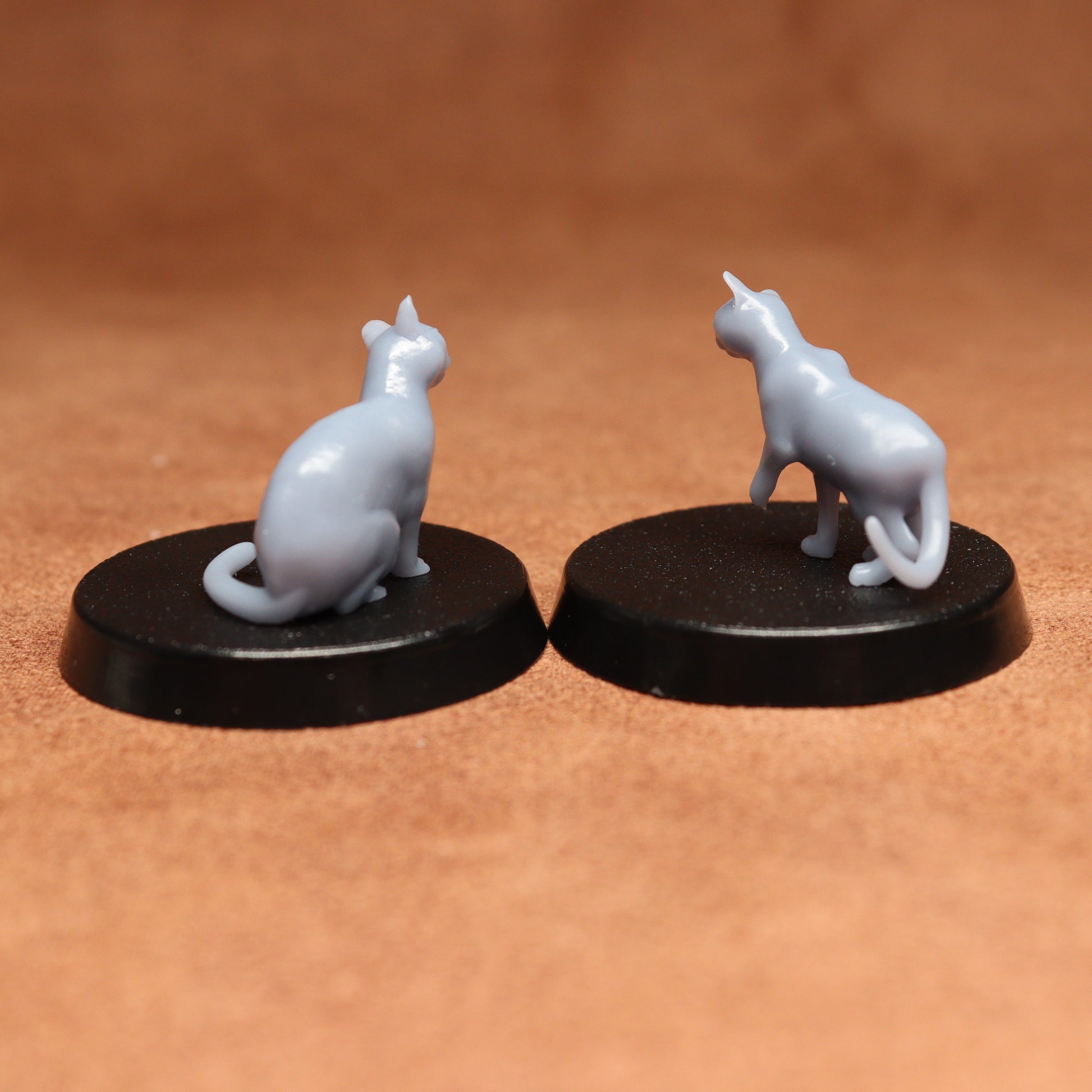 Two miniature cat figurines on black bases against a brown background