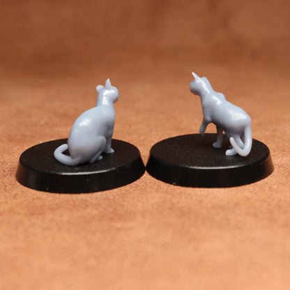 Two miniature cat figurines on black bases against a brown background