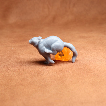 small figure of a cat next to an orange dice on a brown surface