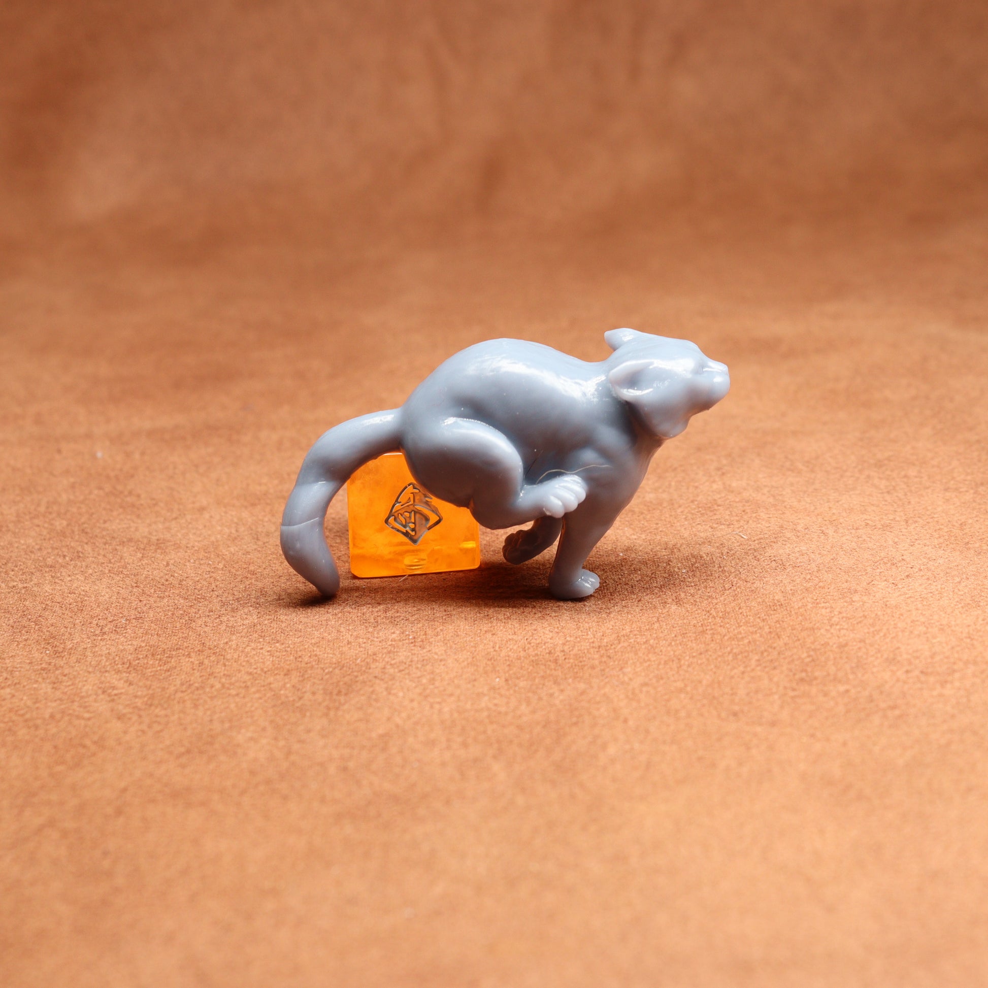 small figure of a cat next to an orange dice on a brown surface