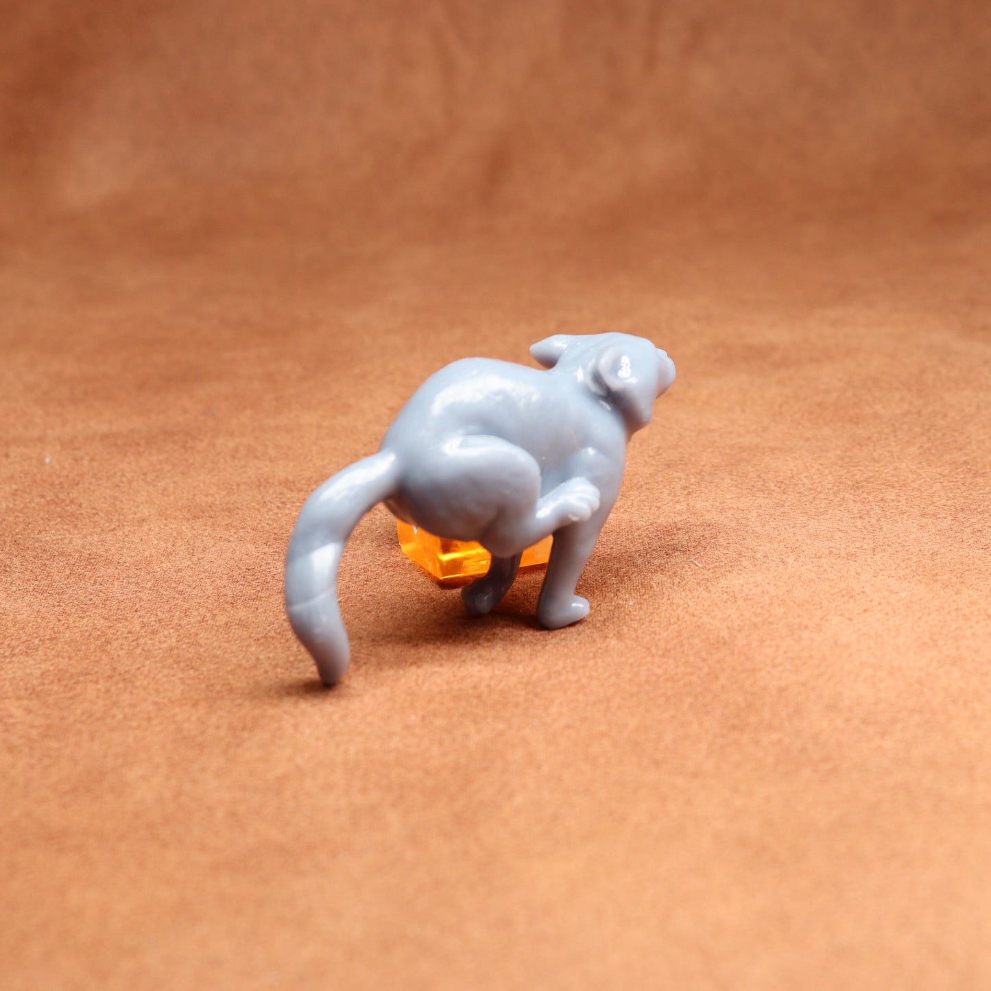 small figure of a cat next to an orange dice on a brown surface
