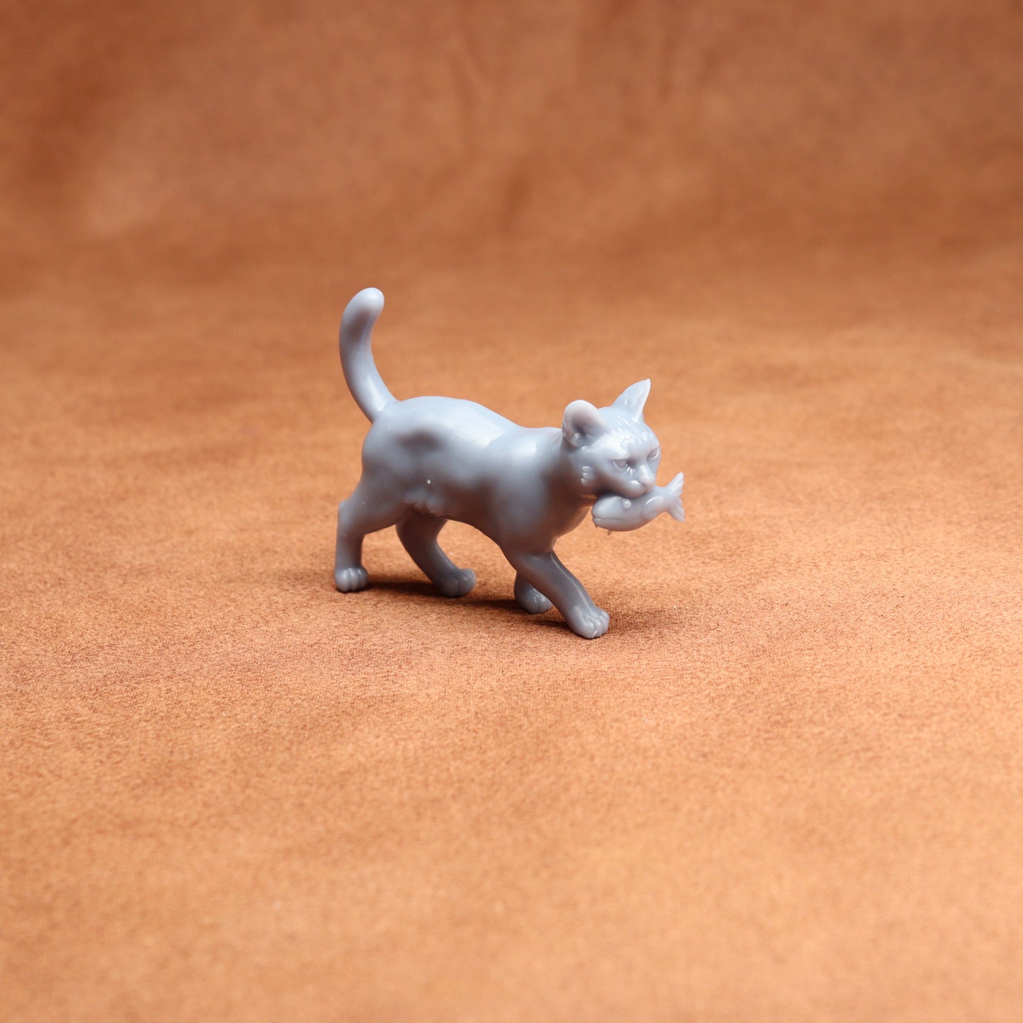 Gray cat figurine holding a fish on a brown surface