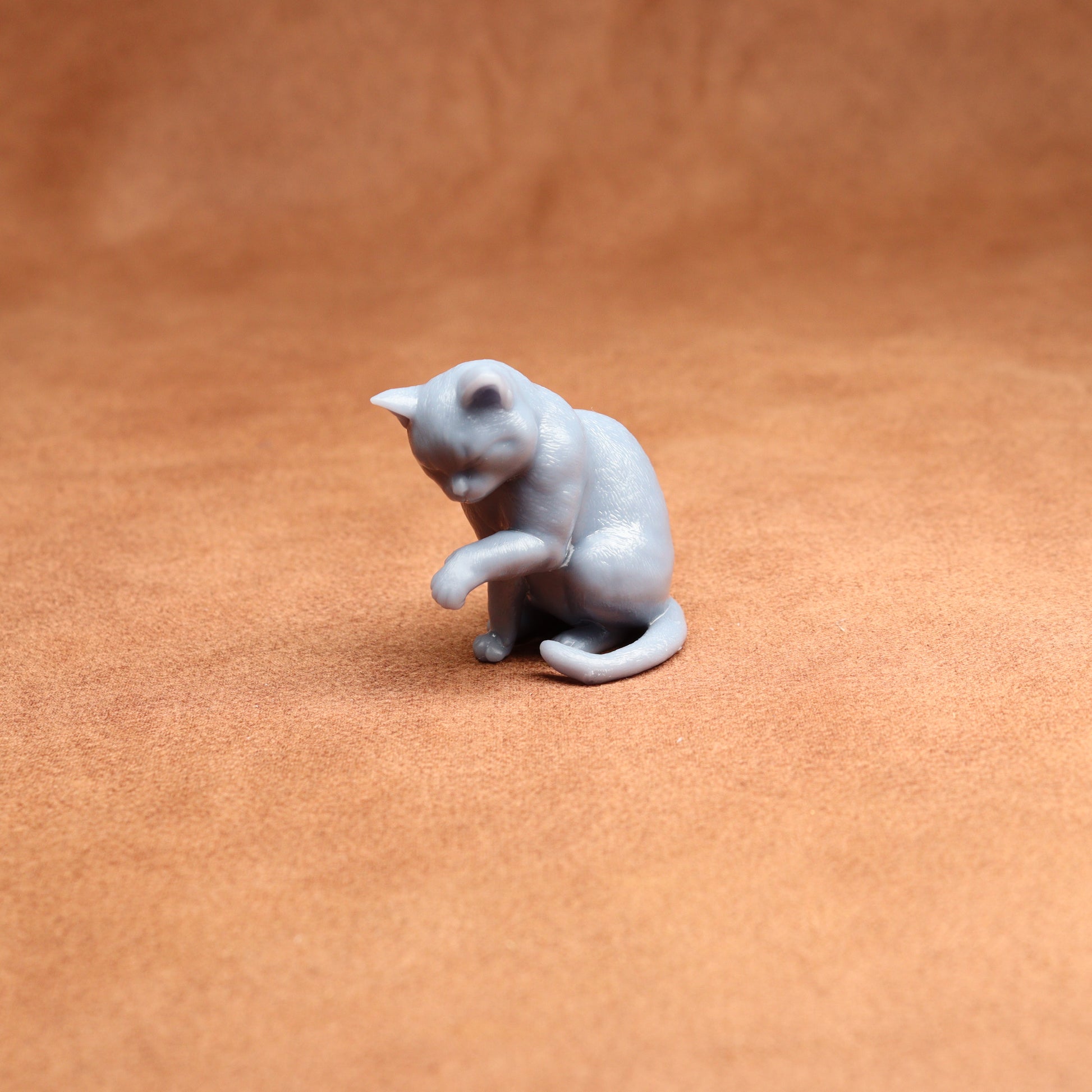 grey resin miniature cat examining its paw on a brown background