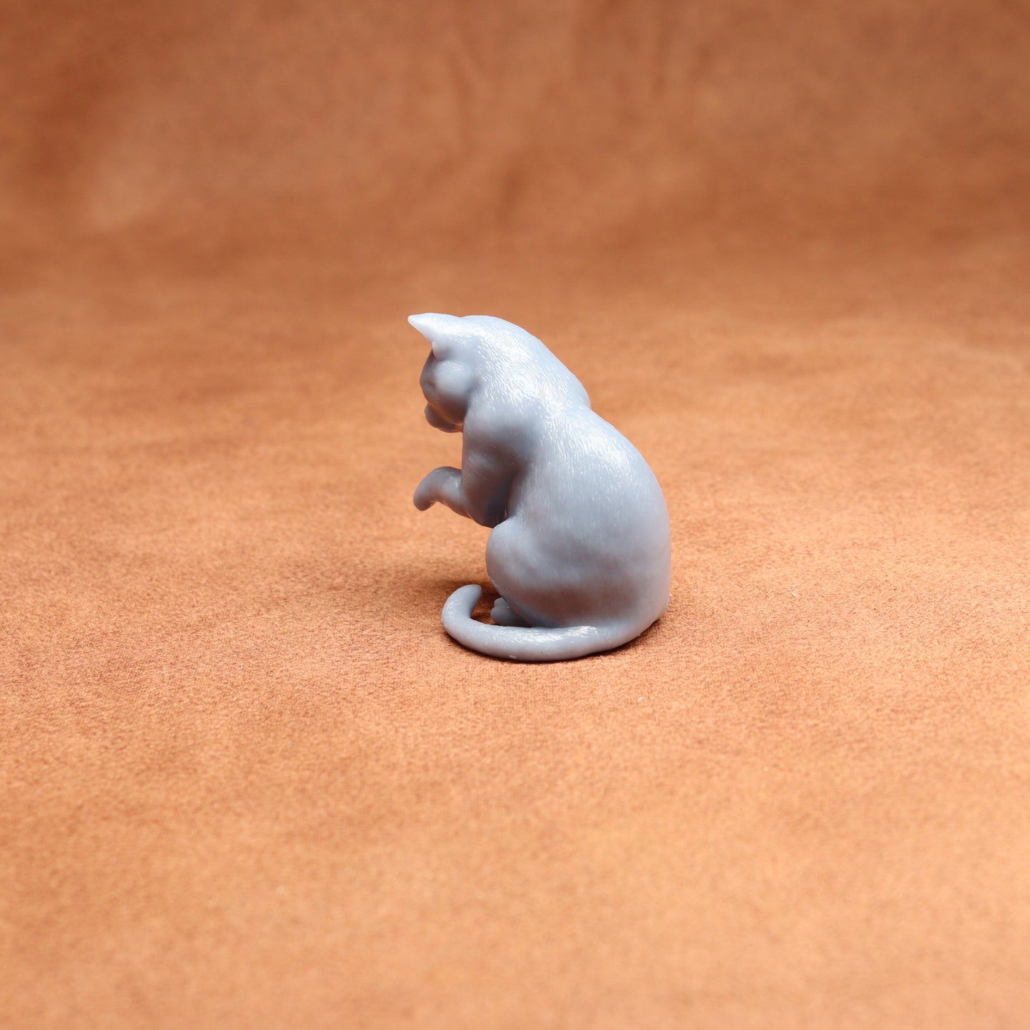 grey resin miniature cat examining its paw on a brown background